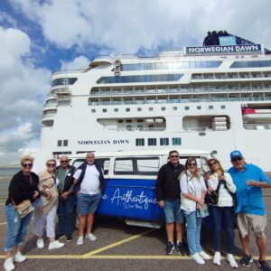 Groupe heureux devant le navire de croisière NORWEGIAN DAWN et un van bleu "The Authentique Wine tours" au port, certains tenant des verres de vin.