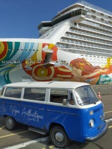 Volkswagen Combi bleu et blanc 'Vigne Authentique Wine Tours' garé devant la coque colorée d'un immense navire de croisière.
